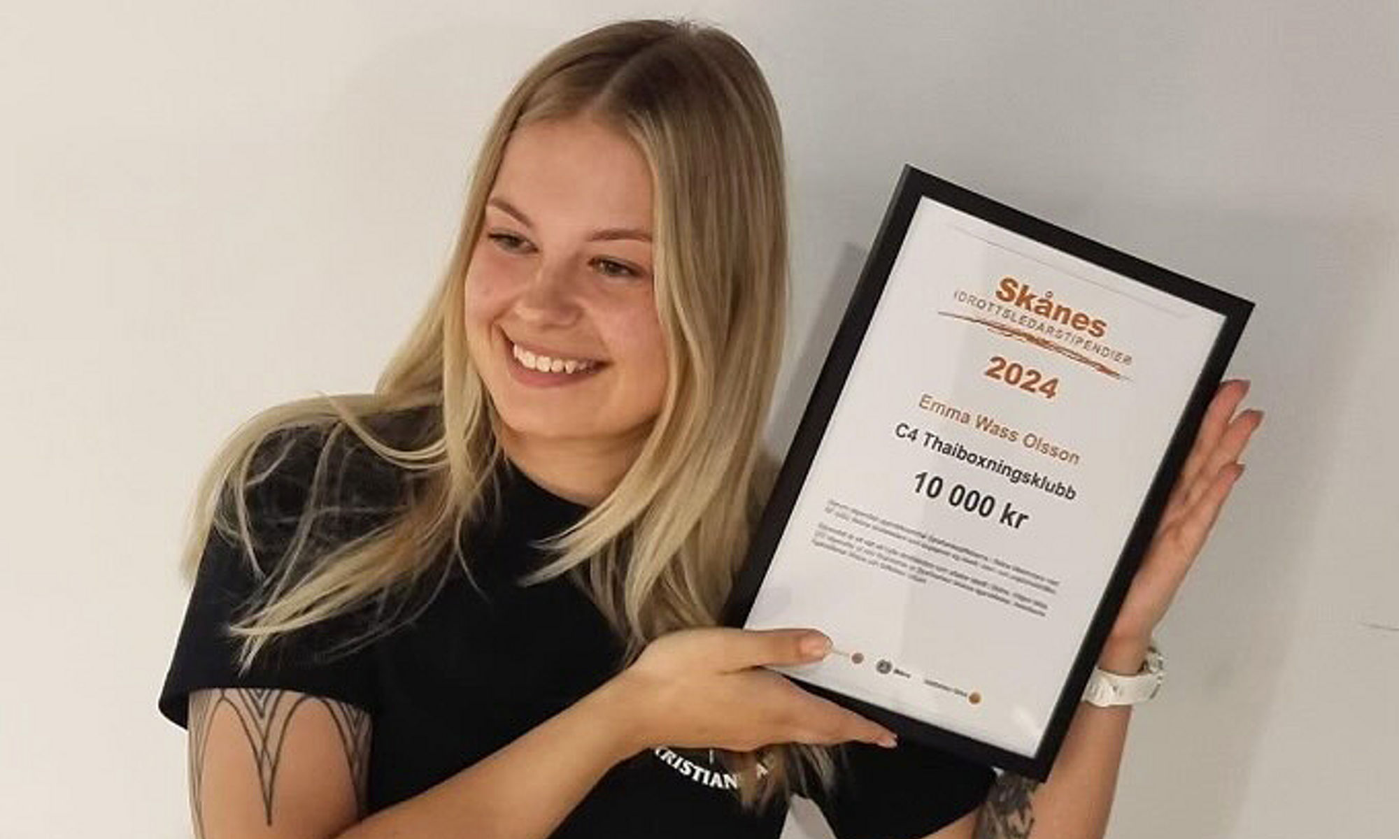 Emma Wass Olsson håller upp sitt stipendium Skånes Idrottsledarstipendier.