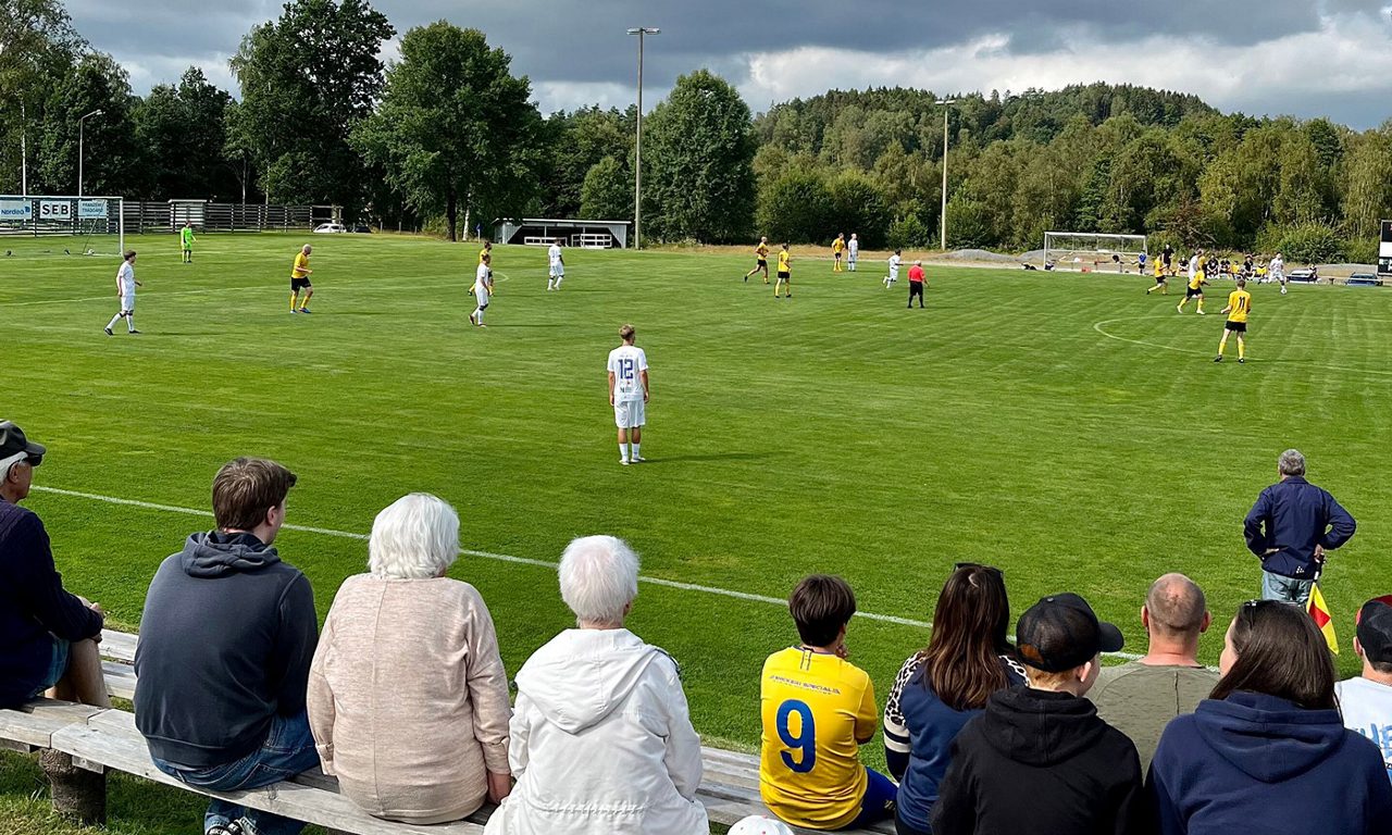 Publik sitter på bänkar framför en fotbollsmatch