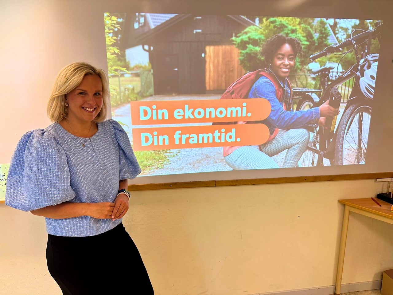 Frida framför en presentation med texten "din ekonomi, din framtid"