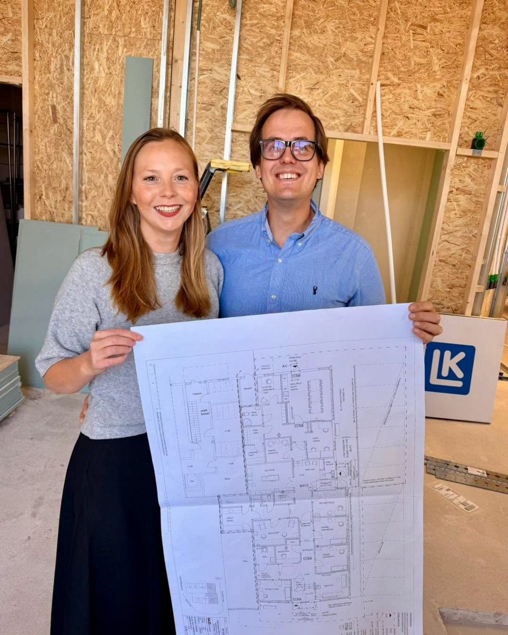 Sanna Unefäldt och Robin Back håller upp en ritning över Grebbestad vårdcentral på byggarbetsplatsen