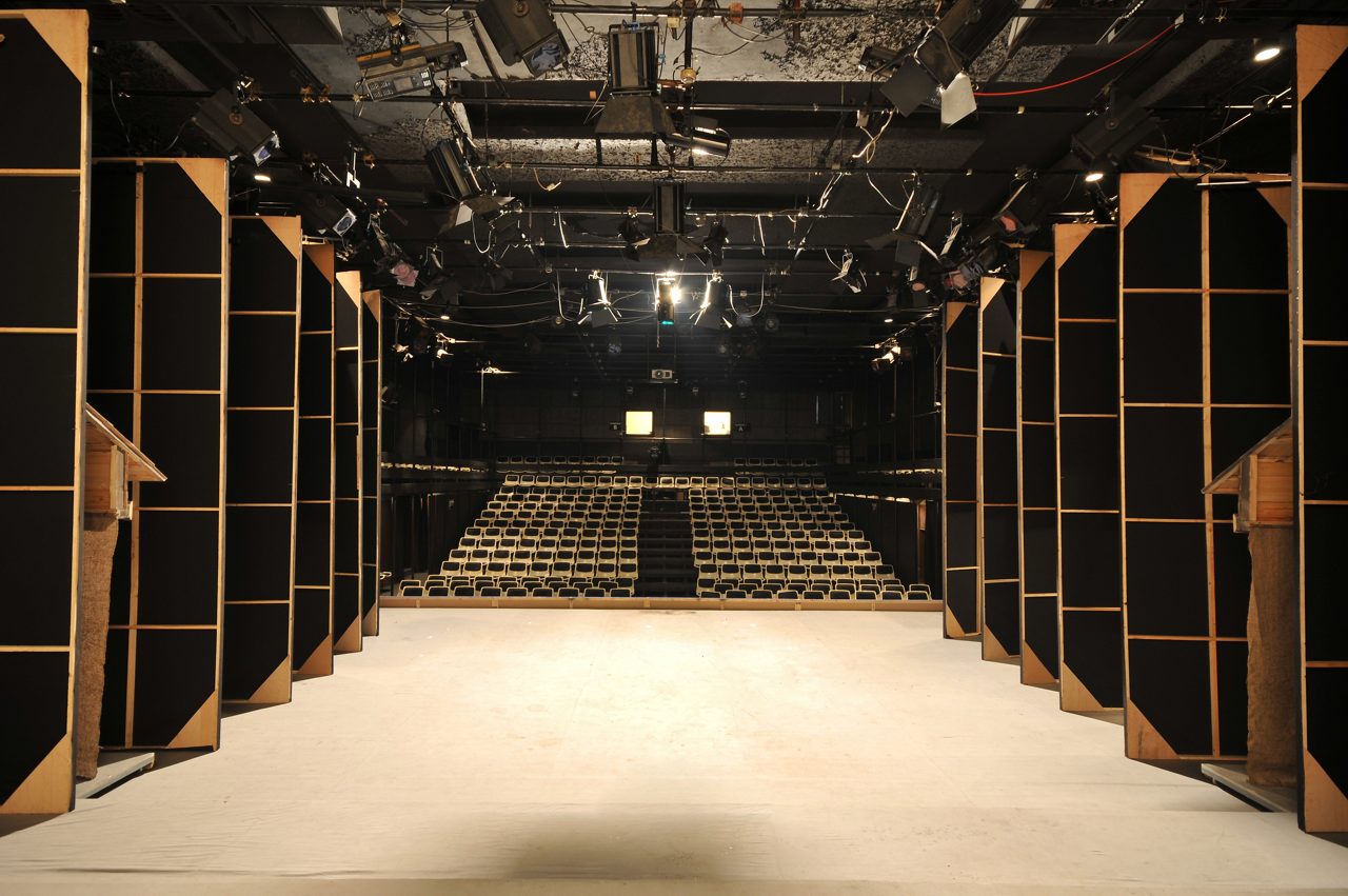 Utsikt från backstage på en liten teaterscen på en utskjuten läktare med många platser