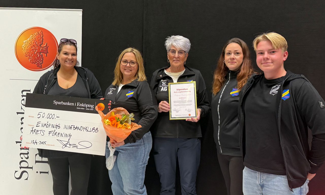 4 kvinnor och en tonårskille iklädd svarta klubbjackor hållandes en stor check från banken, ett diplom och en blombukett