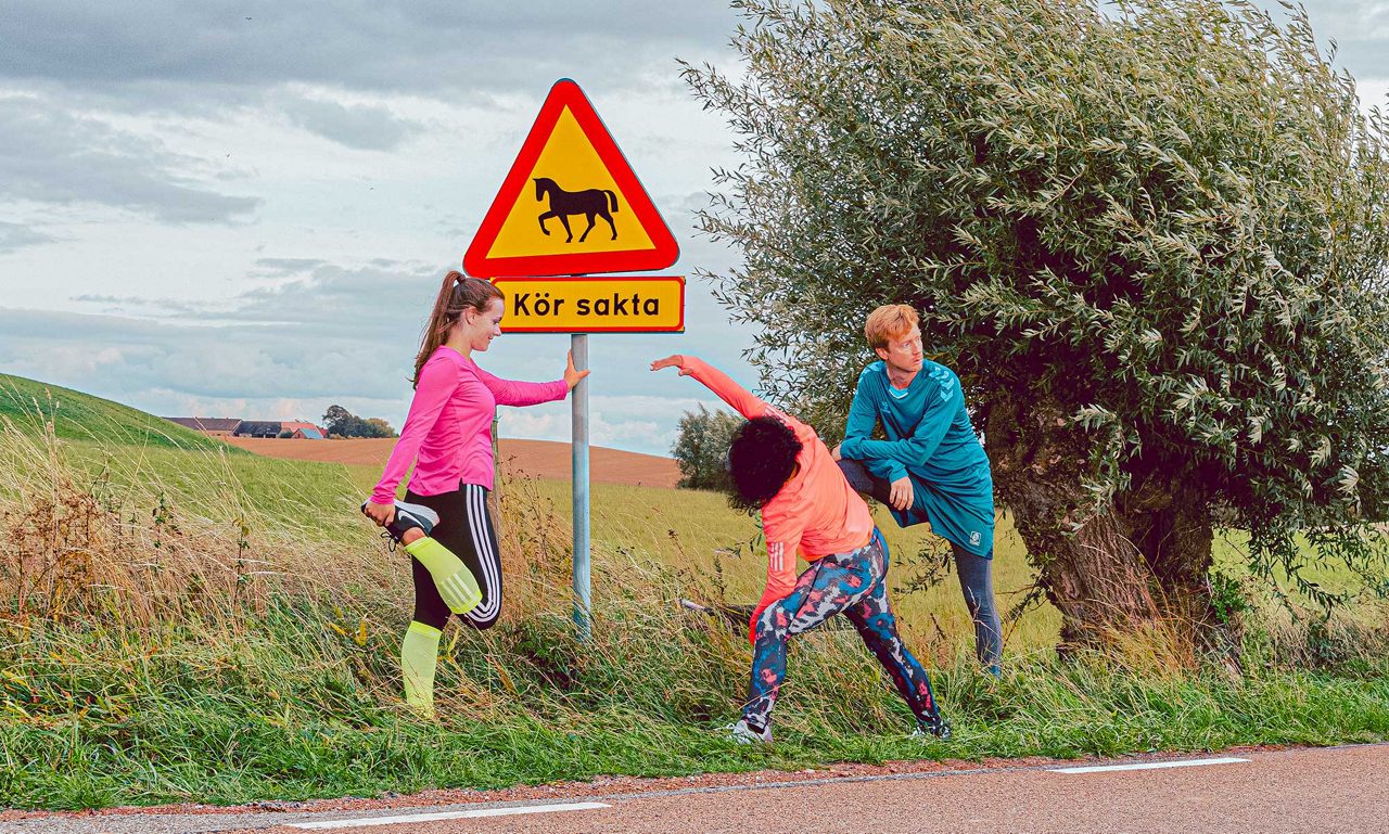En grupp löpare strechar vid en trafikskylt i ett skånskt landskap.
