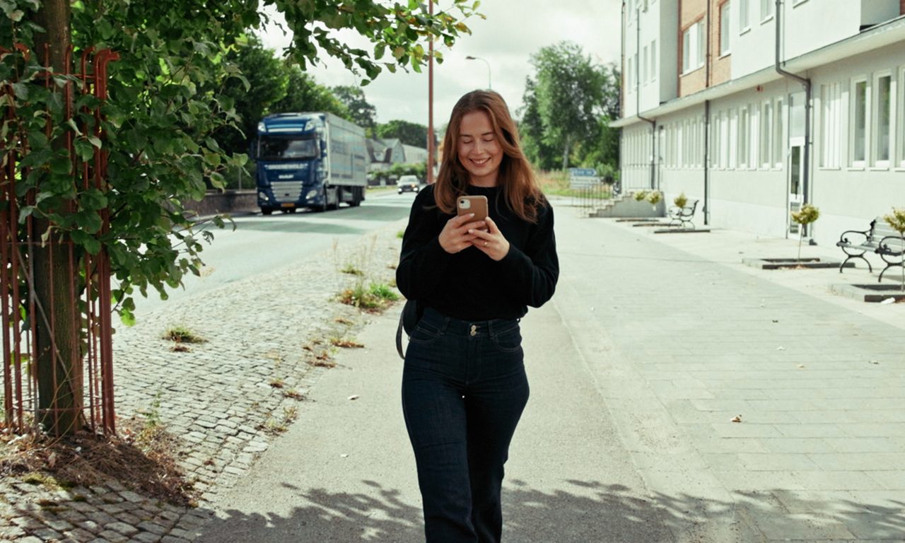 tjej som går på en trottoar. hon tittar ner på sin telefon