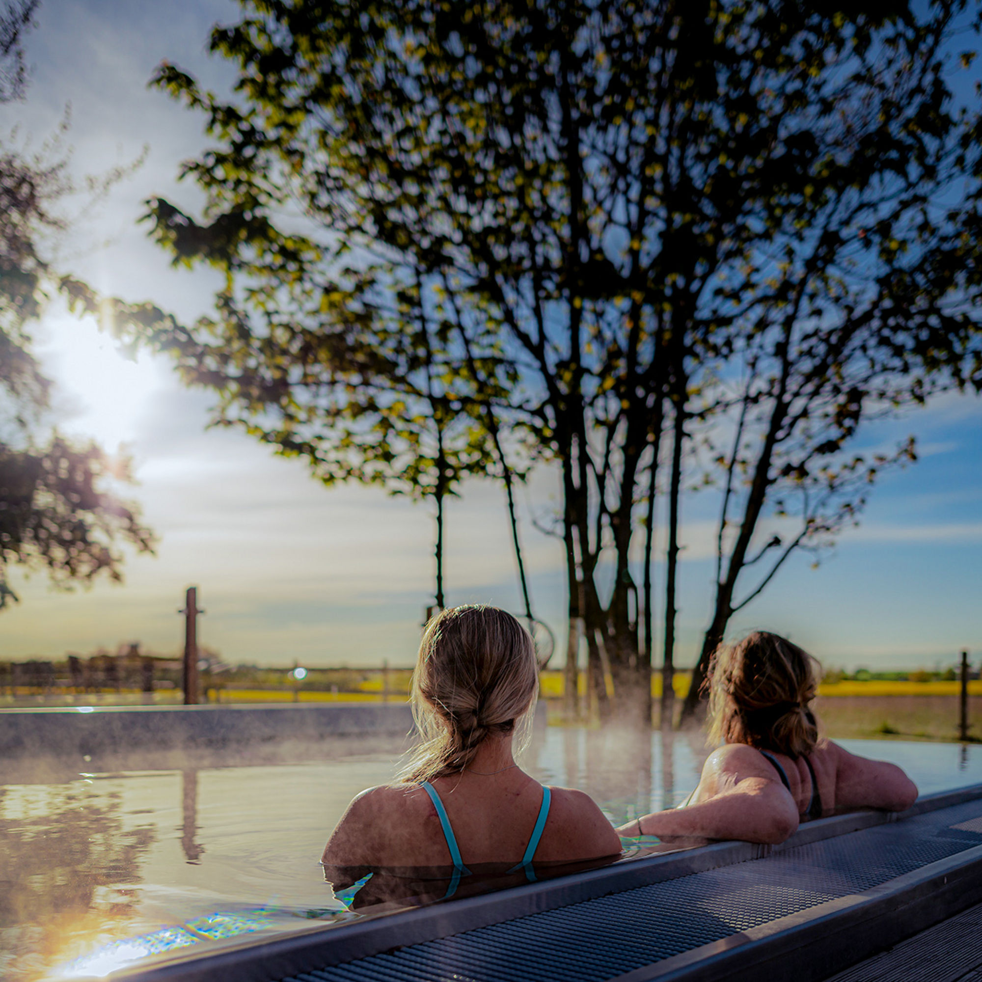 Två kvinnor sitter i en utomhus-pool och blickar ut över det öppna landskapet.