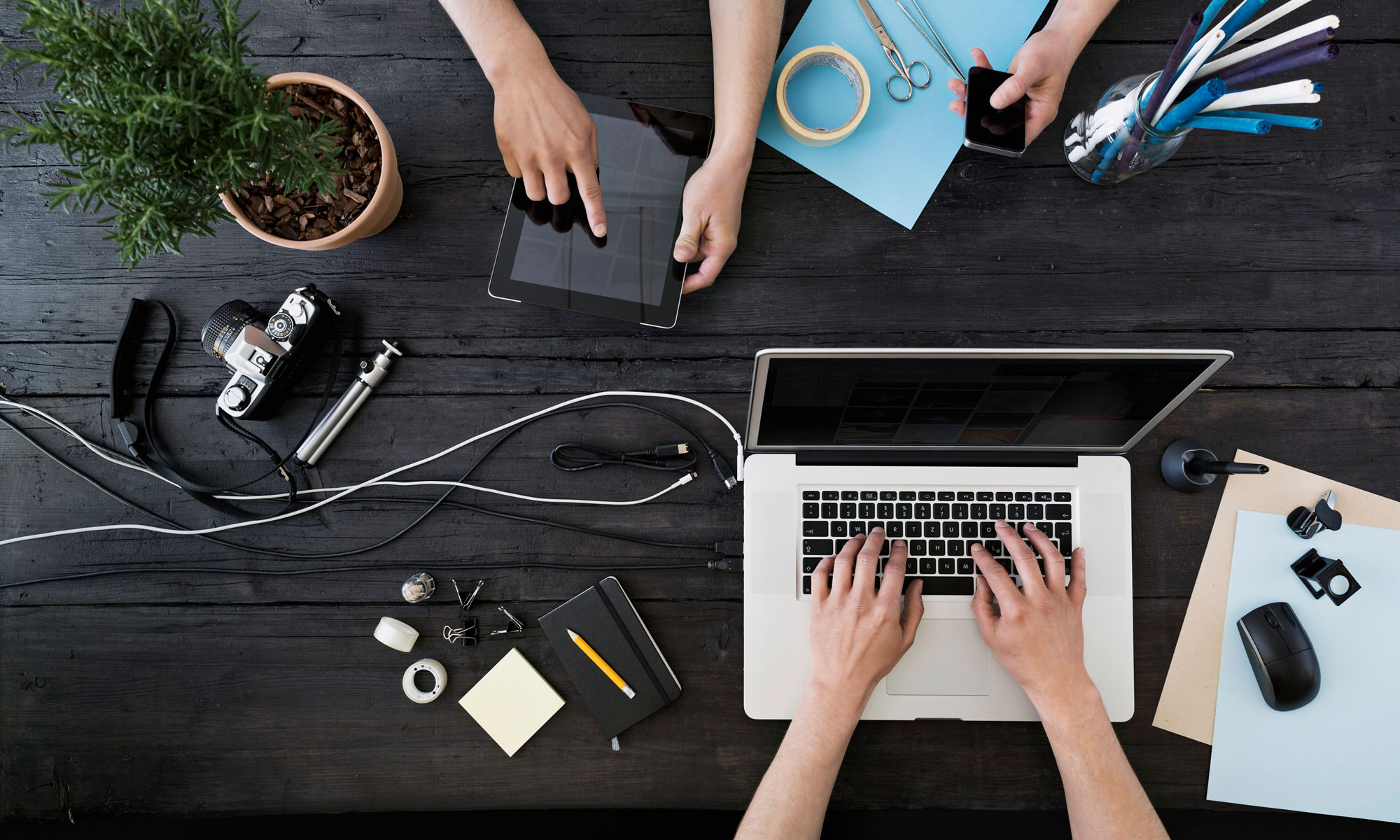 Digitala enheter och papper och pennor på ett bord.