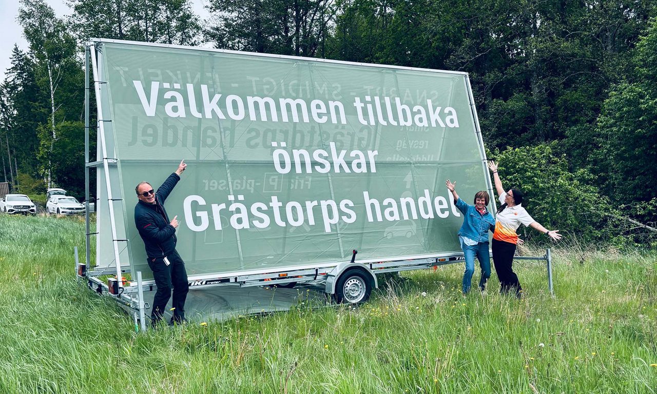 Tre personer står framför en stor skylt