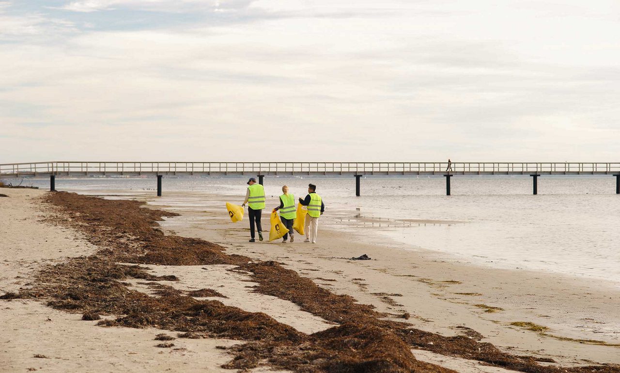 Tre personer går längs en strand med sopsäckar i händerna.