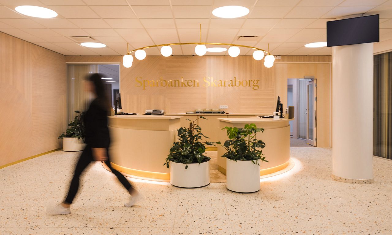 Person passerar förbi kundtjänst på Sparbanken Skaraborgs kontor