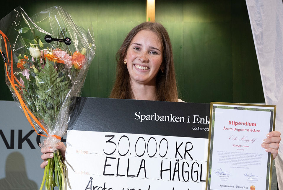 Ung kvinna håller ett stipenidum, en stor check och en blombukett