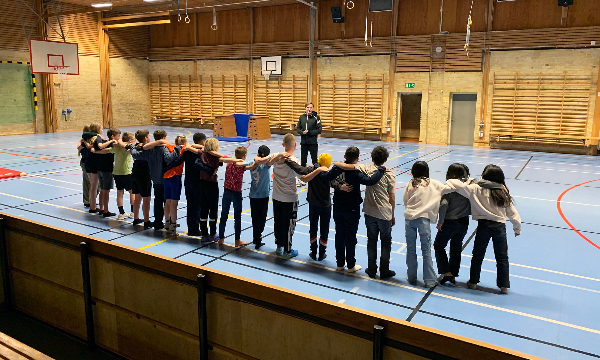 En klass som står i en idrottshall och håller om varandras axlar. 