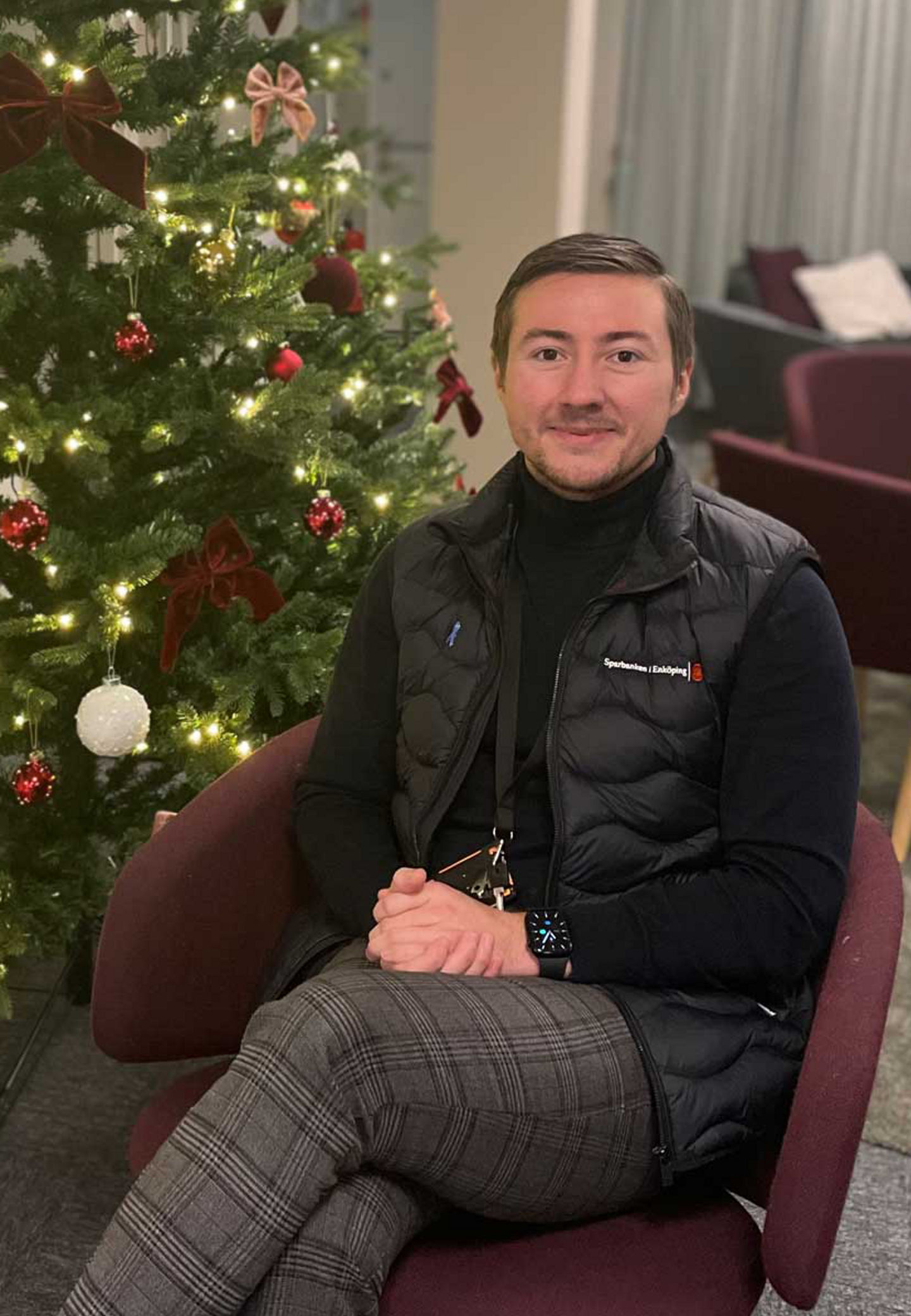 a man dressed in black sitting in front of a christmas tree
