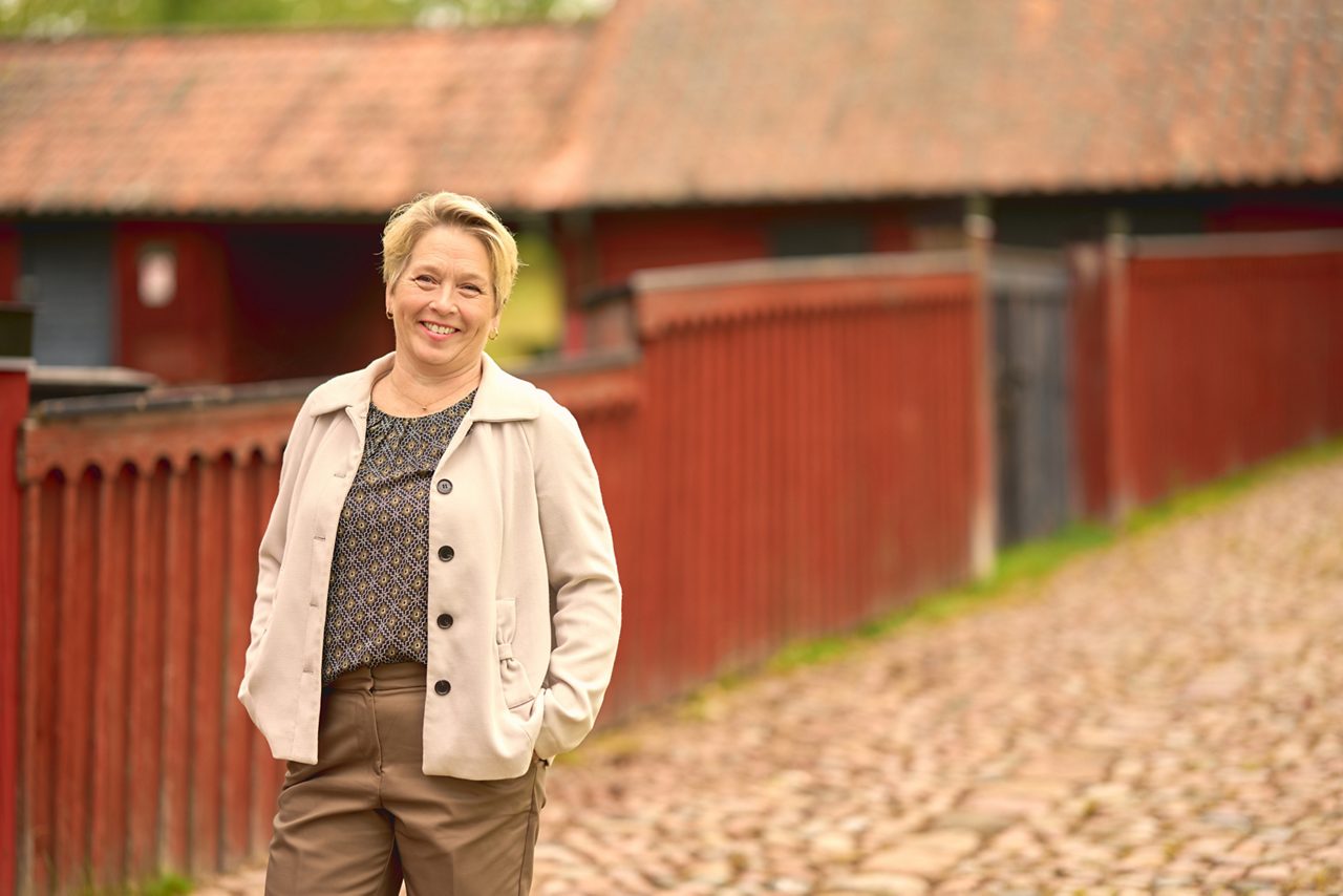 Leende kvinna står framför ett rött staket och röda hus