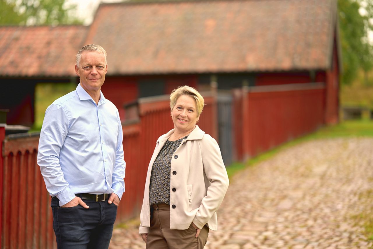 En man och en kvinna står framför ett rött staket och röda hus