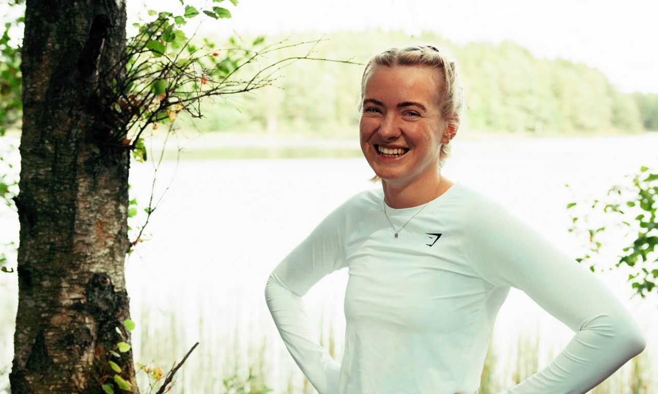 leende tjej som står vid en sjö.