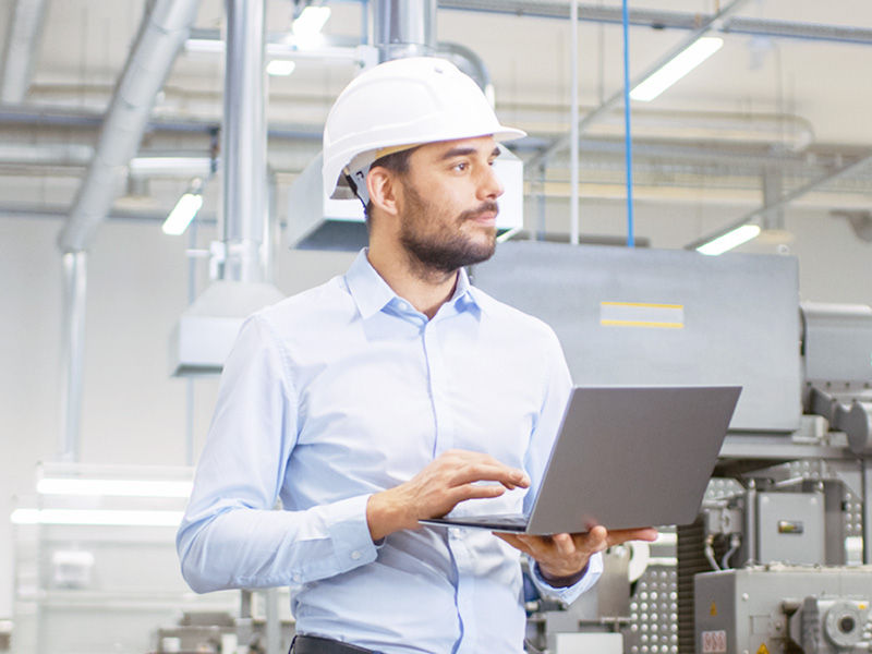 Homme portant un casque de sécurité et utilisant un ordinateur portable pour contrôler les processus de production dans une usine