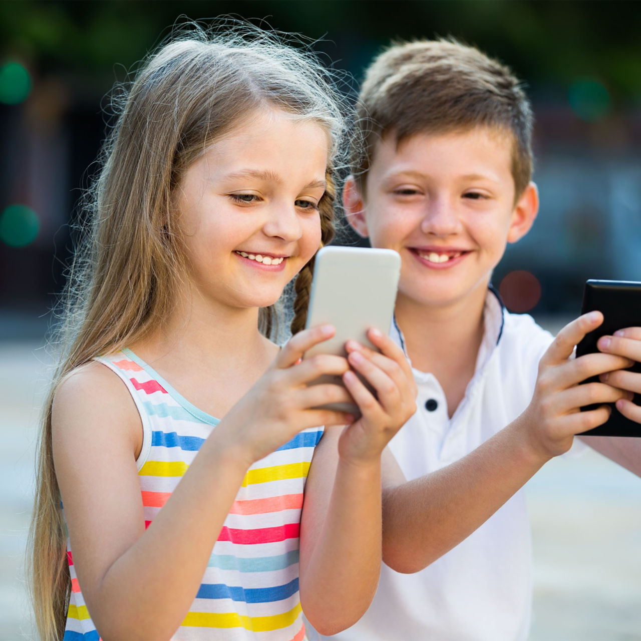  Zwei lächelnde Kinder mit Smartphone