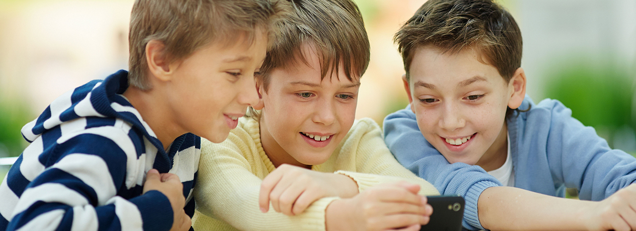 Drei Kinder lachen und schauen zusammen auf ein Smartphone