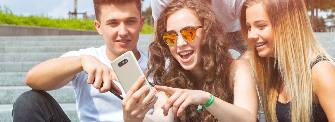 Drei Jugendliche schauen auf ein Smartphone am Seeufer