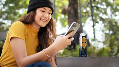 Girl looking at phone, coffee drink in Tetra Pak carton