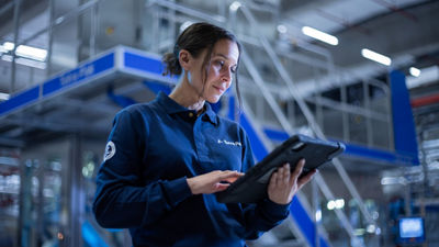 Une femme dans une usine tient une tablette, concentrée sur l'écran.