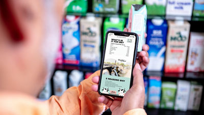 Mit Smartphone vorm LEH Regal gefüllt mit Milch
