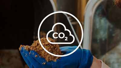 Gloved hands holding plant-based material with a CO2 emissions symbol