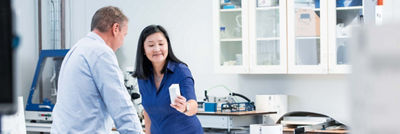 Uma mulher e um homem examinam uma embalagem em uma instalação de laboratório.