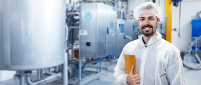 Homem com touca e roupa de proteção em pé com iPad na fábrica