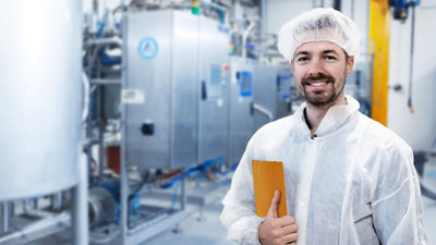 Homem com touca e roupa de proteção em pé com iPad na fábrica