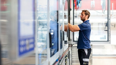 A technician in a blue polo shirt operating industrial machinery in a bright manufacturing facility.