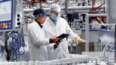 Two employees reviewing a tablet beside a conveyor carrying cartons