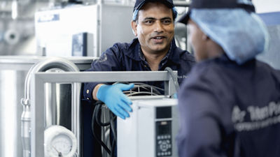 A man wearing blue standing by a machine and talking to a woman