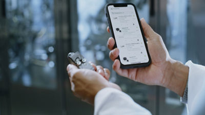 In einer Hand ein defektes Ersatzteil, in der anderen Hand das Smartphone mit dem Shop um es nachzubestellen.