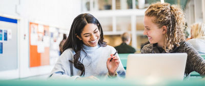 Two women sit in front of an open laptop engaged in a lively conversation.