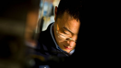 An image of a person with glasses and a focused expression, working on a task with a dimly lit background.