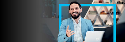 Un uomo professionista con un blazer blu sorridente e impegnato in una conversazione mentre tiene un laptop in un ufficio moderno.