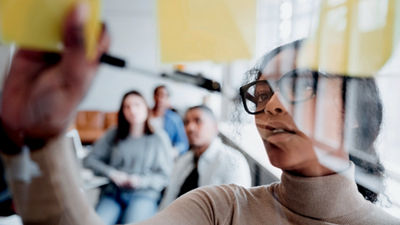 Une femme présente des notes autocollantes à un public engagé dans le cadre d'une discussion.