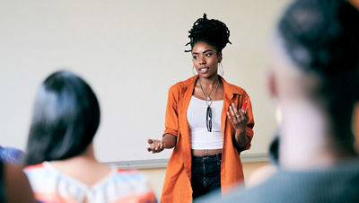 Une femme se tient à l'avant d'un groupe de personnes qui échangent des idées.