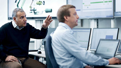  Two men work in front of several computer screens.