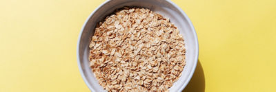 Bowl filled with rolled oats on a bright yellow background.