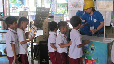 Geri dönüşüm standının önünde temizlenmiş ve düzleştirilmiş kartonlarla okul çocukları