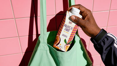 On-the-go juice Hand placing a passion fruit drink carton into a reusable shopping bag