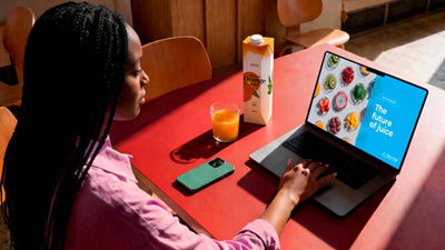 Woman watching a juice webinar on a laptop while drinking juice