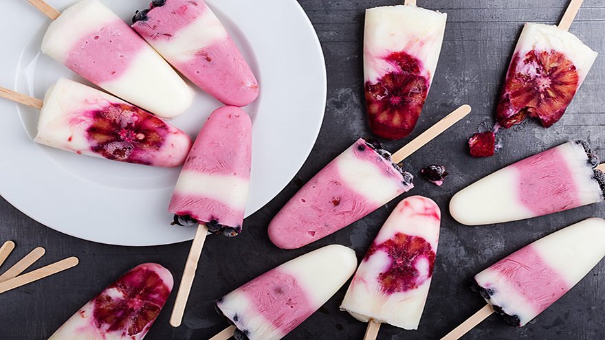 Food background. Homemade berry yogurt ice pops with frozen black currant and blood orange slices on rustic gray table, high angle view