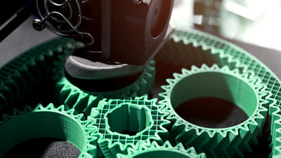 Detail view on print head of 3D-printer making a planetary gear part from mint coloured plastic