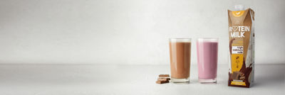 Two glasses with flavoured milk, proteing milk in Tetra Prisma Aseptic carton package