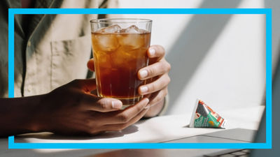 Hands with iced tea in glas and triangle package on the table.