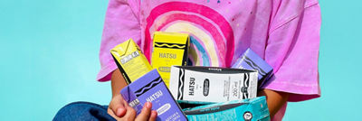 Person in pink t-shirt holding Hatsu tea packages.