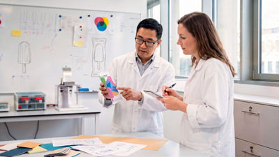 Two people in lab coats examine ice cream packaging samples in a laboratory.